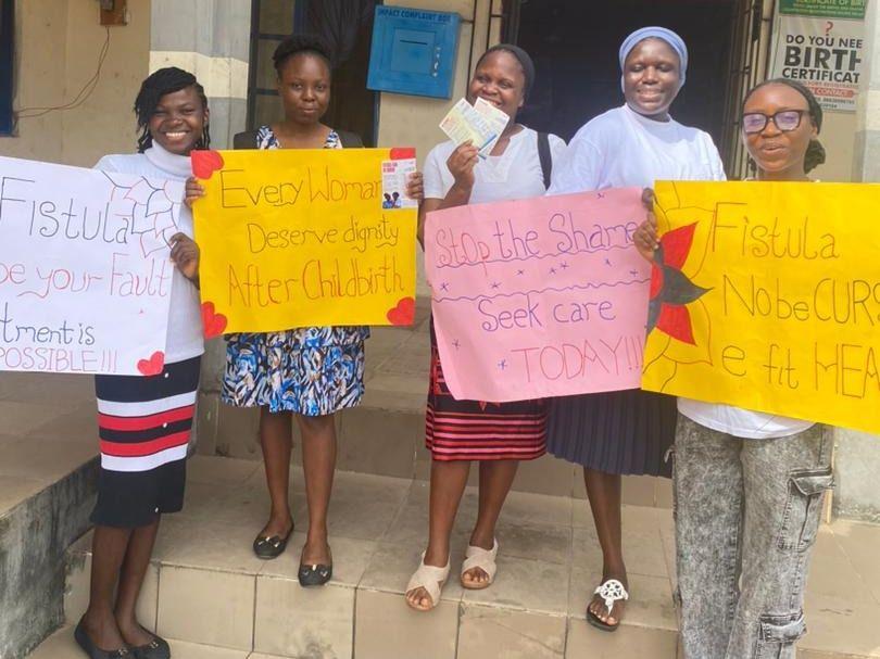 FCI volunteers outside a health centre hold signs saying every woman deserves dignity after childbirth